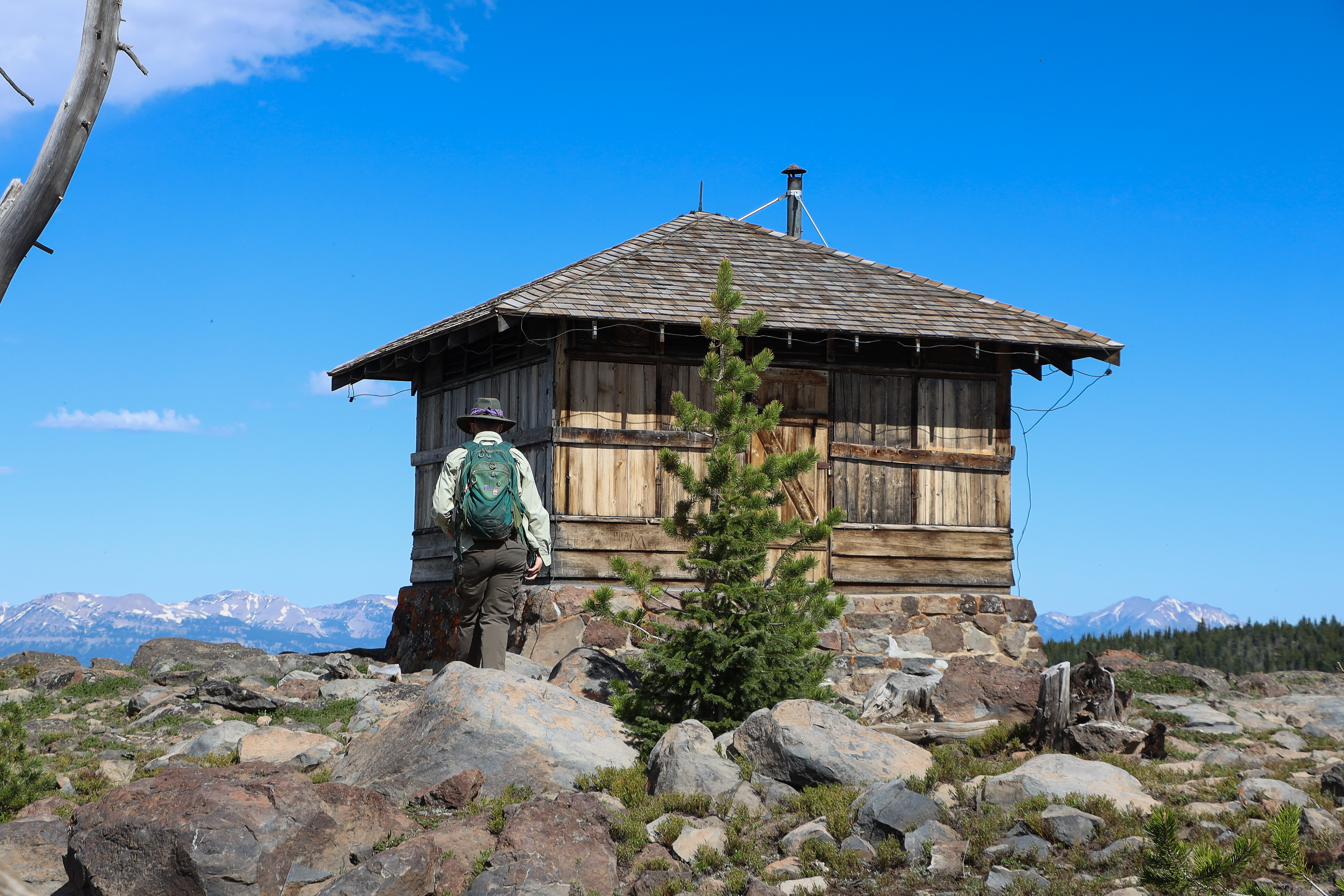 A hiker approaches a fire lookout on top of a mountain.
