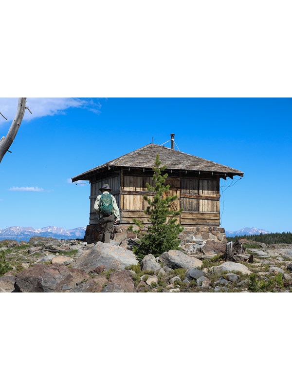 A hiker approaches a fire lookout on top of a mountain.