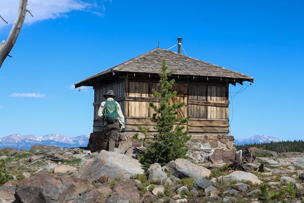 A hiker approaches a fire lookout on top of a mountain.