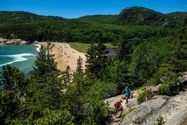 Two hikers walk along Great Head Trail overlooking Sand Beach.