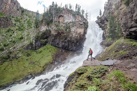 A hiker stands at the base of a large waterfall.