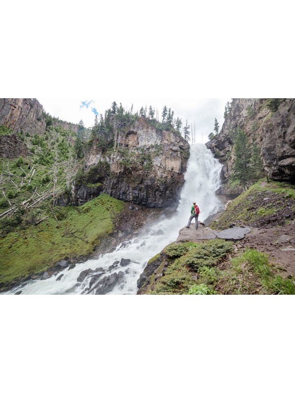 A hiker stands at the base of a large waterfall.