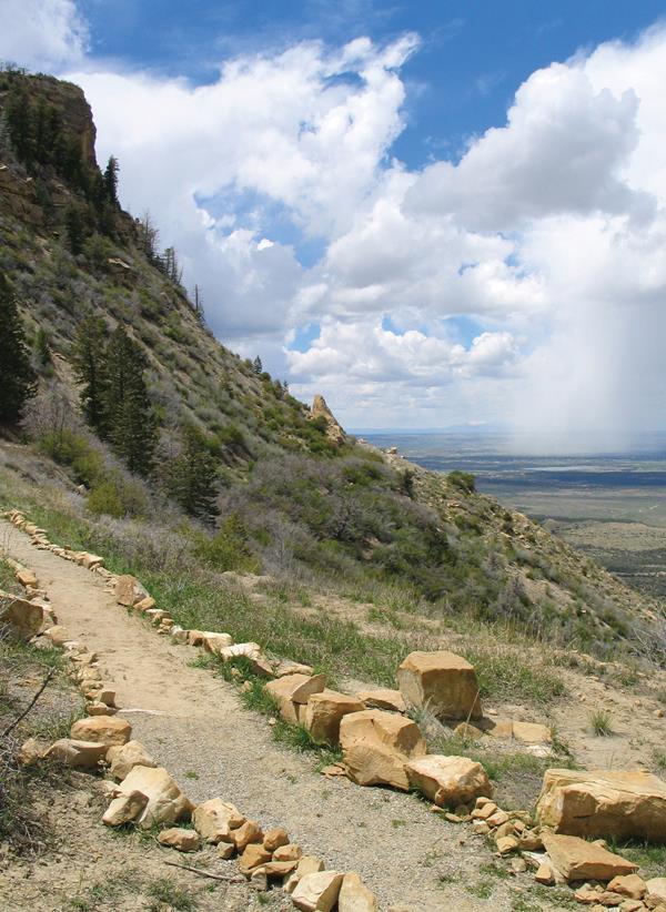 Dirt trail, lined with stones, traverses a ridge with view of a green valley in the distance below.