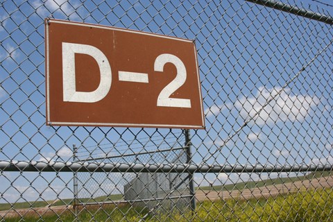 Brown sign with the inscription "D-2" on a chain-link fence