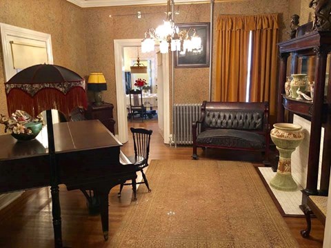 The parlor room with a tall lamp, baby grand piano, couch and vase surrounding the room