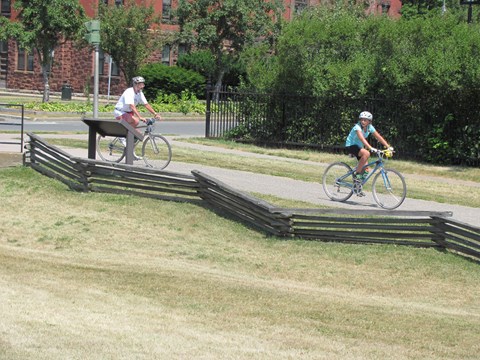 Two people cycle in a line down the park trail.