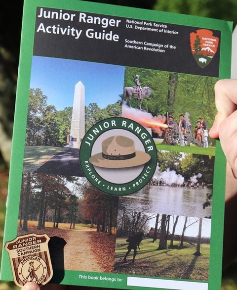 The cover of a junior ranger booklet with the wooden badge held in the lower left corner.
