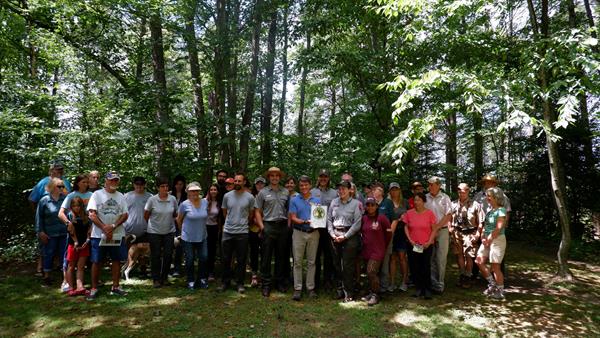 A group of 34 people with 3 park rangers posing in front of trees in a forest.