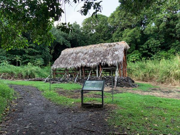 A traditional open air Hawaiian building stands upon a lava rock foundation.