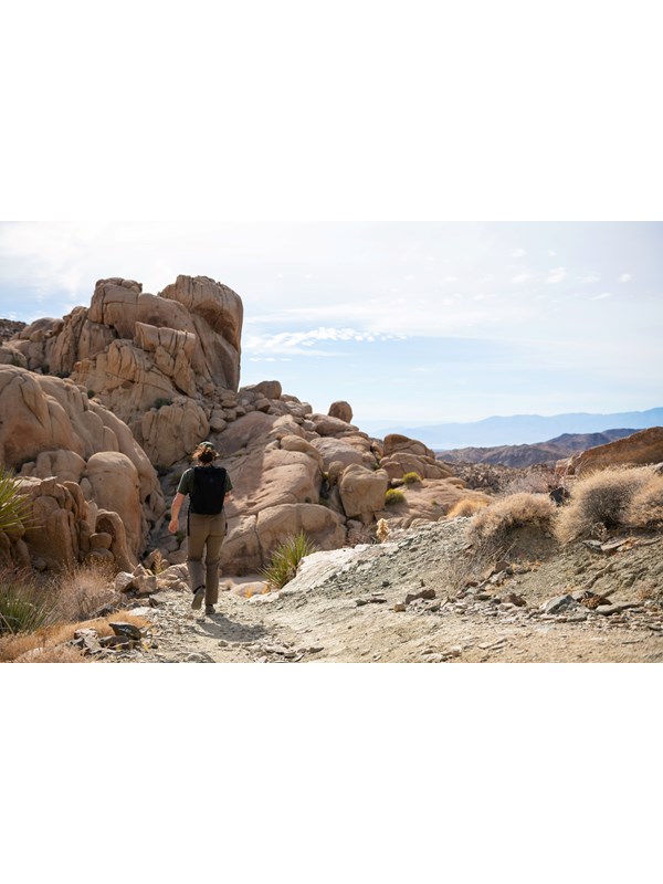 A hiker on a dirt trail headed towards a large rock formation in the distance.