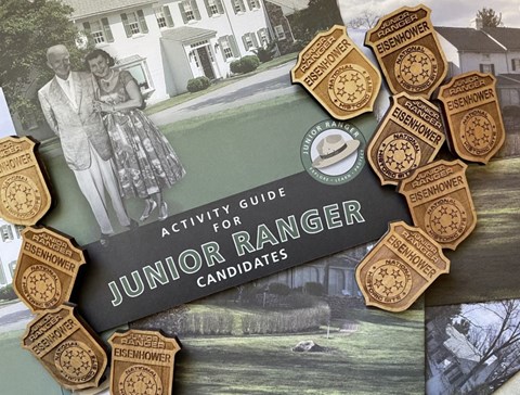 A color image showing a green and black book with brown wood JR Ranger badges