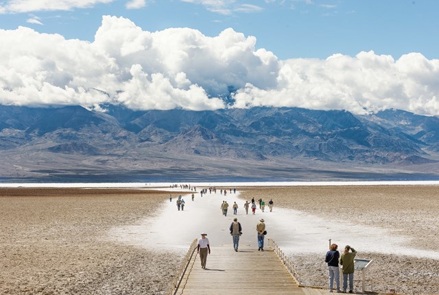 The image shows a broad, arid landscape with a wooden path leading deep into a salt flat.