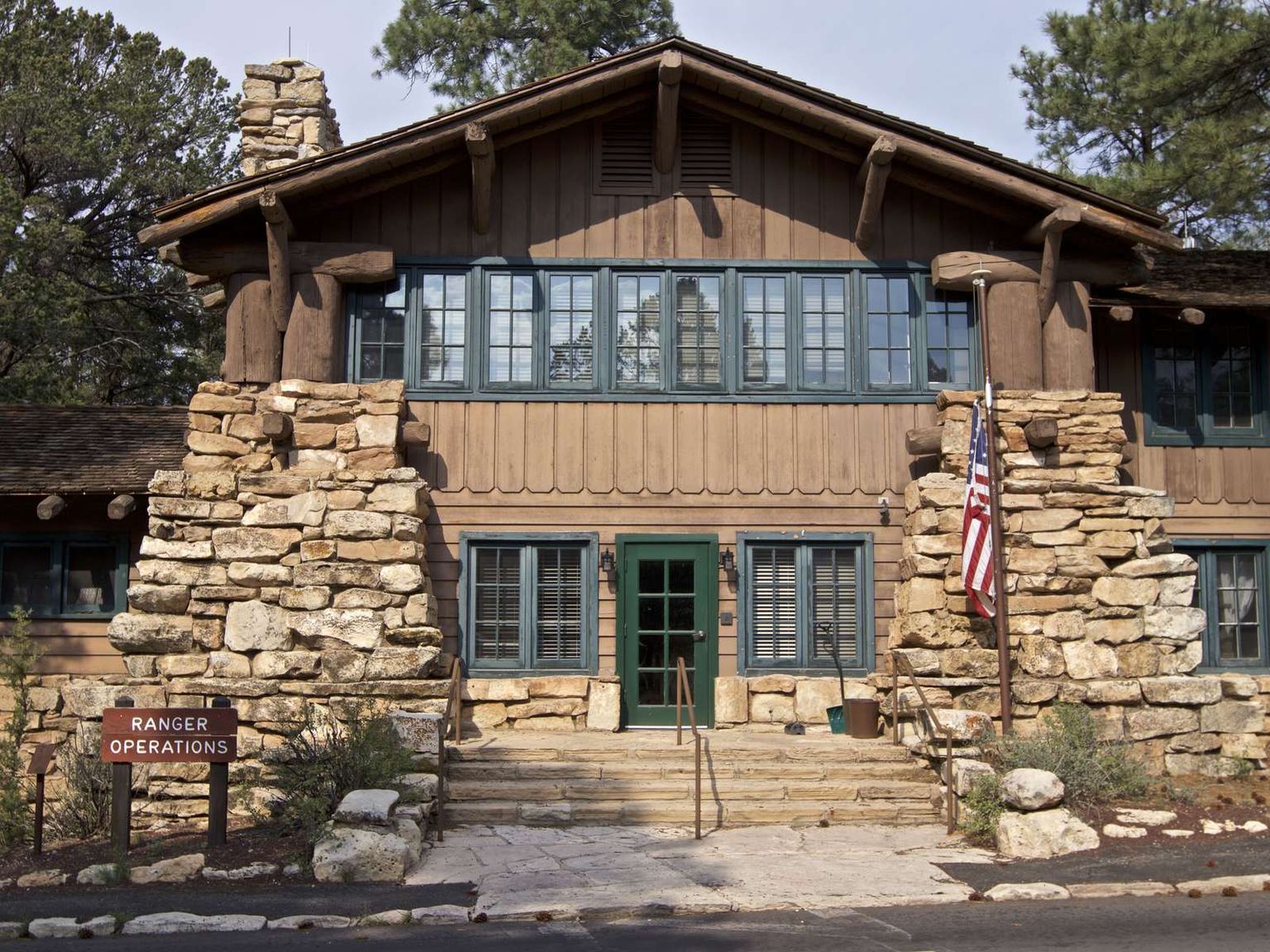 A two story wood and stone building with steps and an USA flag out front