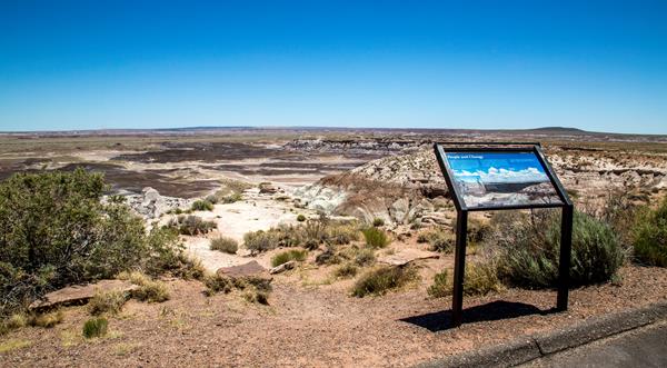 View of mesas, escarpment, floodplain, with wayside exhibit under a blue sky.