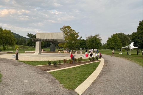 People gathered around a large bronze bell with grass, trees, and trails throughout