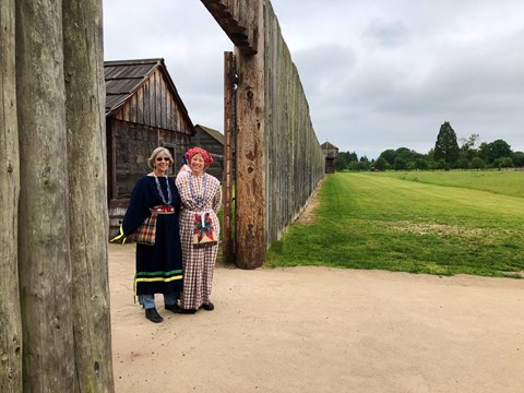 The gates of Fort Vancouver with two women in 1840s style clothing standing in front.