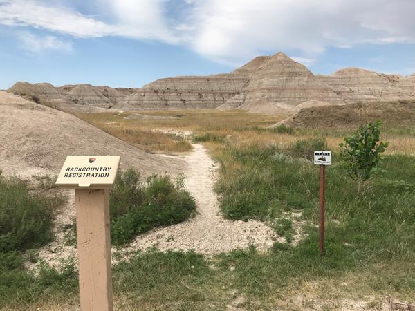 A game trail extends out from between a registration kiosk and "beware rattlesnakes" sign.