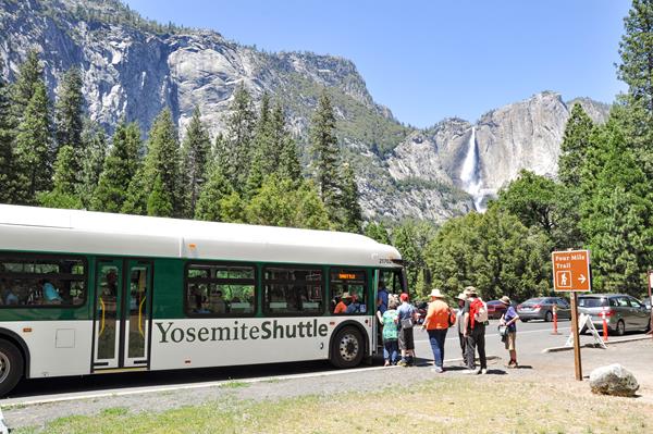 People boarding shuttle bus at Four Mile Trailhead with Yosemite Falls in the background.