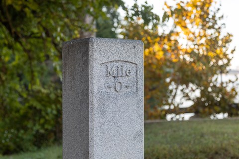 Granite post carved Mile 0 with autumn trees blurred behind