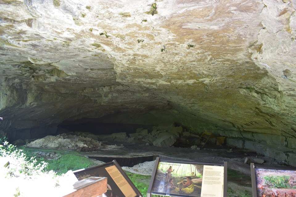 A low rock ceiling hangs over a dug pit and several informational signs