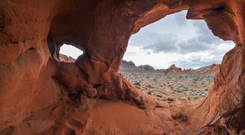Looking out of a cave in a rock formation out into a desert landscape.