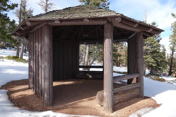 Wooden gazebo with green wooden shingle roof in snowy forest