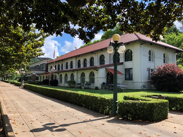 A white stucco building with a red tiled roof sits behind a short green hedge.