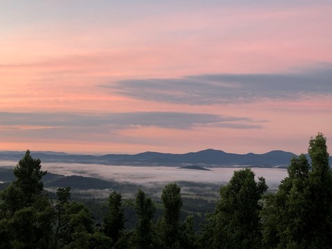Image of a colorful sunrise viewed from Afton Overlook. Low clouds hang over the valley below.