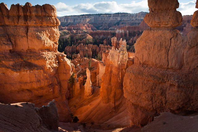 A glowing landscape of red and orange rock spires and forest seen from above