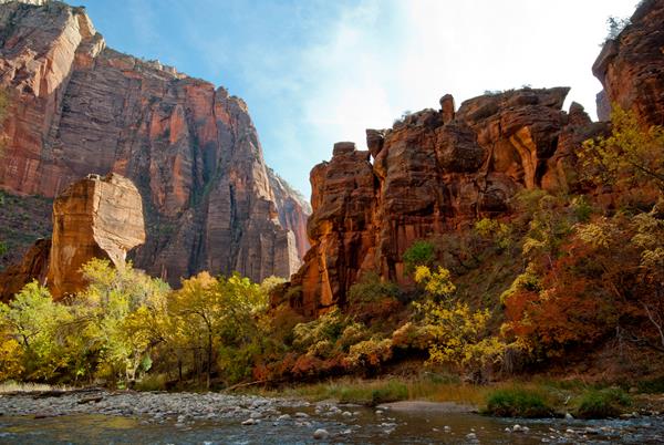 A redrock sandstone formation under blue skies, with a clear river running in front of it.