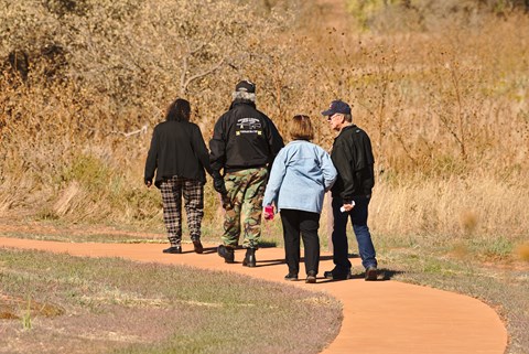 Four people walking a paved trail through a grasslands