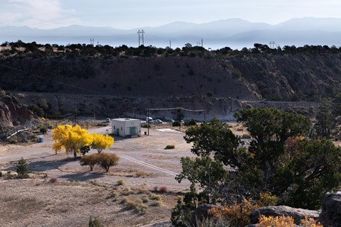A small white building sits on a concrete pad in a valley surrounded by cliffs and sagebrush hills.