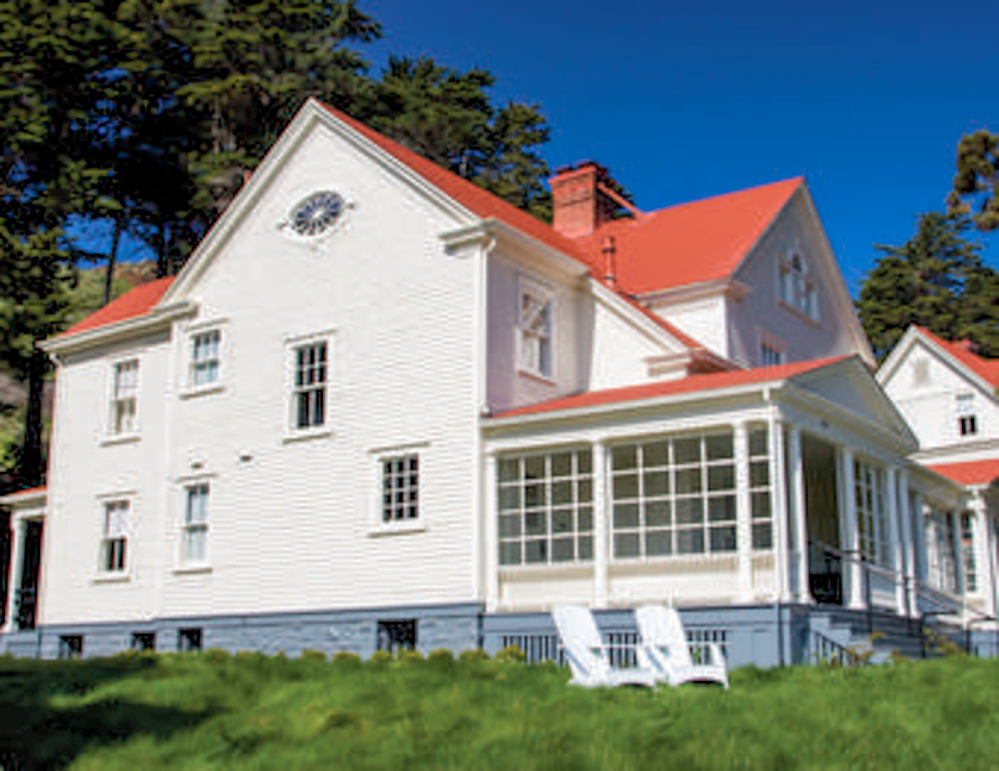 Colored photo of an officer's house with a red roof and white siding. In front are two white chairs.