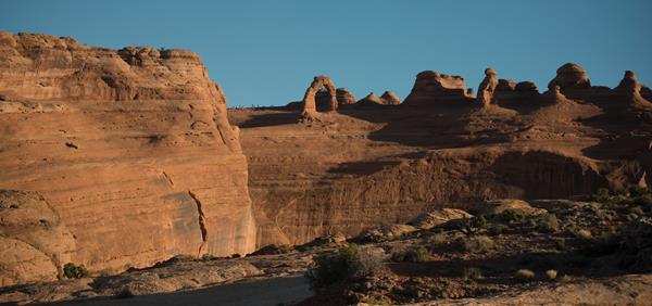 A free-standing sandstone arch and other rock features, viewed across a canyon.