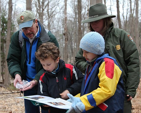 Two adults and two children in a woodland setting look over a map.