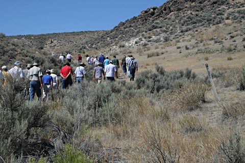 People walk up a through a sage brush covered ravine.