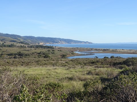 Grass and scrubland in the foreground, wetlands in the mid-distance, and rugged coastline beyond.