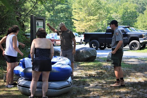 Three visitors stand next to sign with a stack of inner tubes. A park ranger speaks to them.