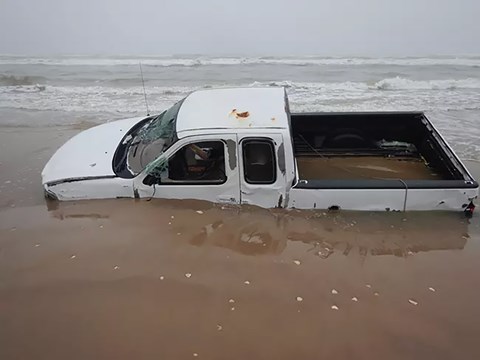 A white truck stuck in wet sand on a beach.