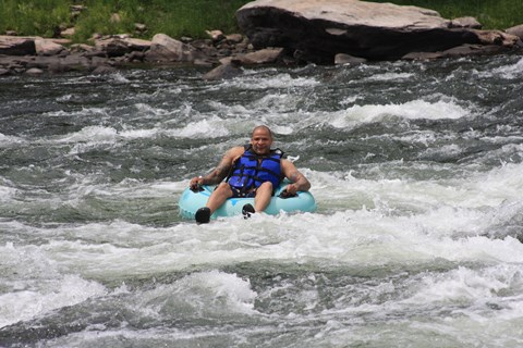 man in life jacket and blue inner tube floats through white-water rapids