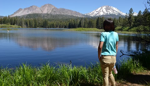 A looks out on a brush-lined lake backed by volcanic peaks.