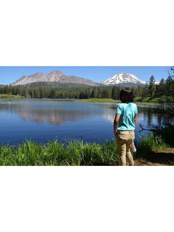 A looks out on a brush-lined lake backed by volcanic peaks.