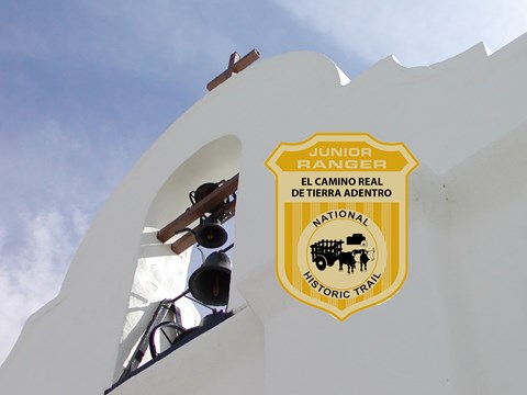 A junior ranger badge over a white stucco church bell tower.