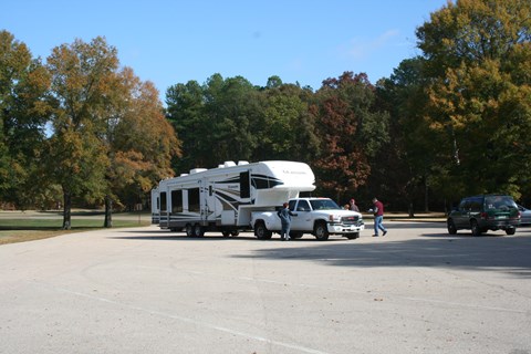 A large white pick up truck pulling a 5th wheel camper is parked in parking lot.