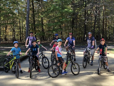 Ten men and boy cyclists pose with their road bikes, wearing helmets and smiling