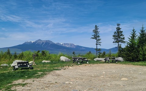 Three picnic tables sit facing an expansive view of neighboring Katahdin on a sunny day.