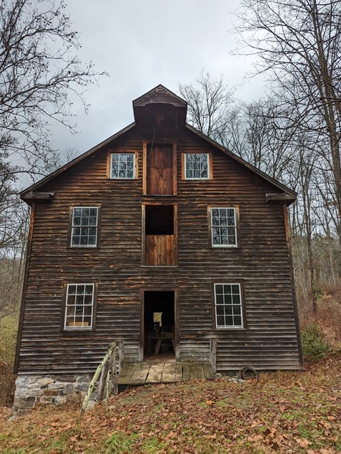 A wooden grist mill three stories tall surrounded by fallen leaves.