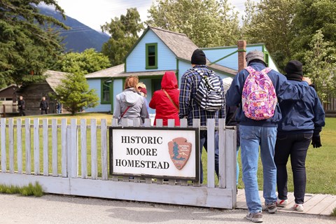 People gathered in front of a house with fence sign "The Moore Homestead"
