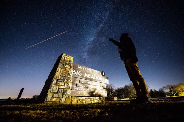 A person points up to the Milky Way Galaxy in the sky over the sign for Big Meadows.