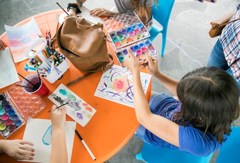 a child sitting at a craft table working on watercolors